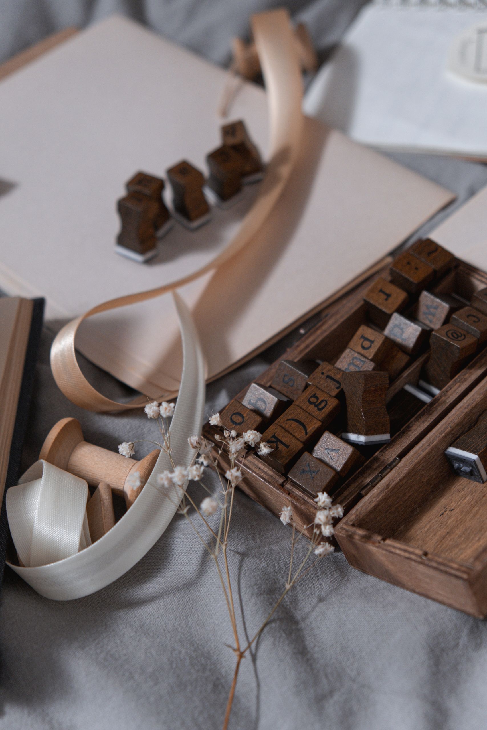 Artistic setup of wooden letter stamps, ribbons, and dried flowers on a soft background.